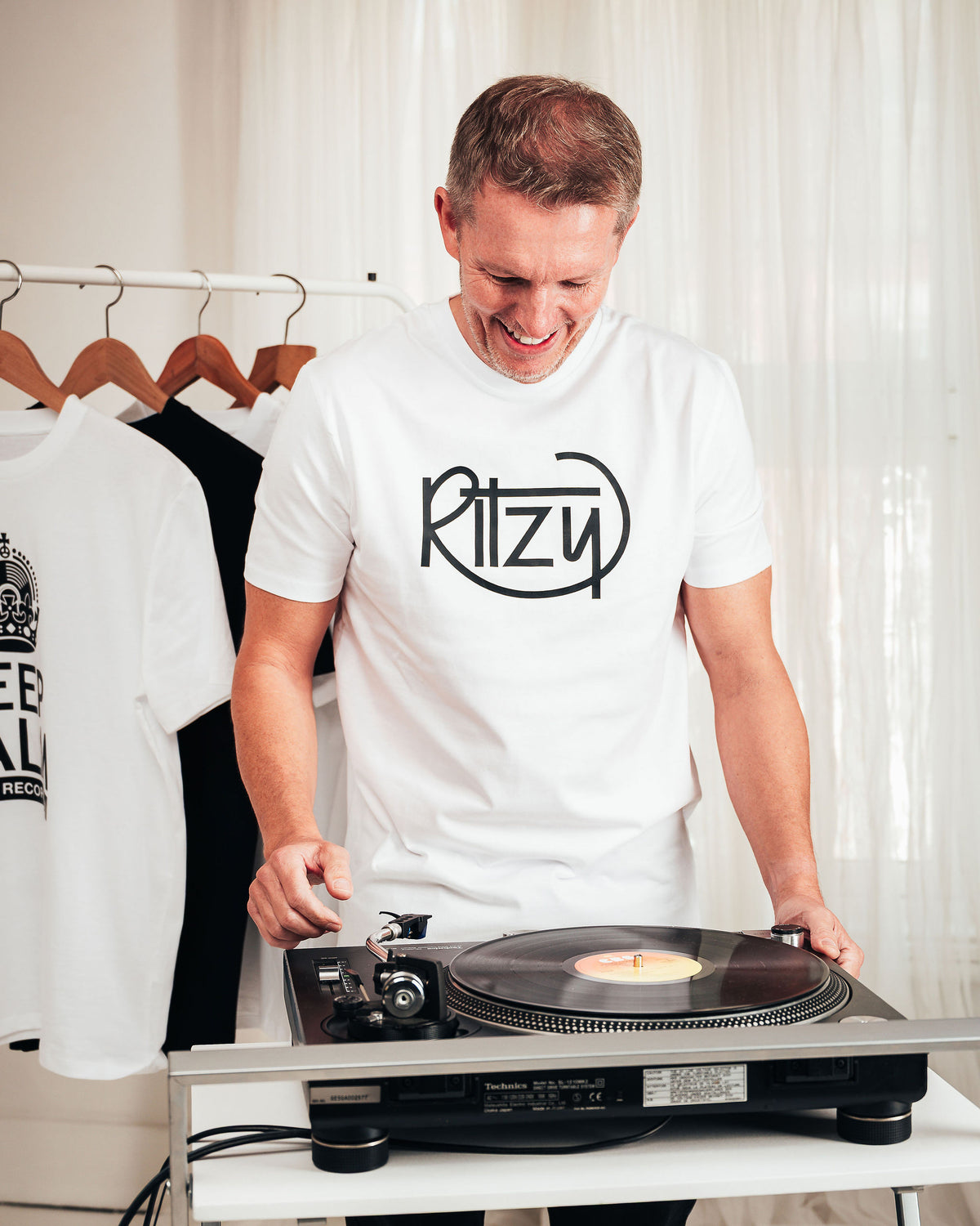 Jason smiling at a turntable wearing a white Ritzy T-shirt.